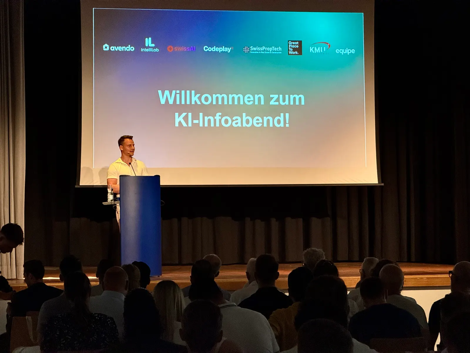 Speaker auf der Bühne beim KI-Infoabend in Suhr, im Hintergrund die Willkommensfolie mit den Partnerlogos